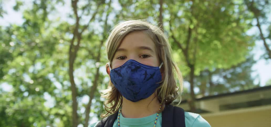 Portrait of a child standing outside wearing a face mask and carrying a backpack