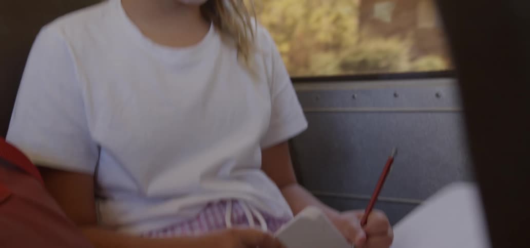 A girl with a notebook and a pen sitting on a bus