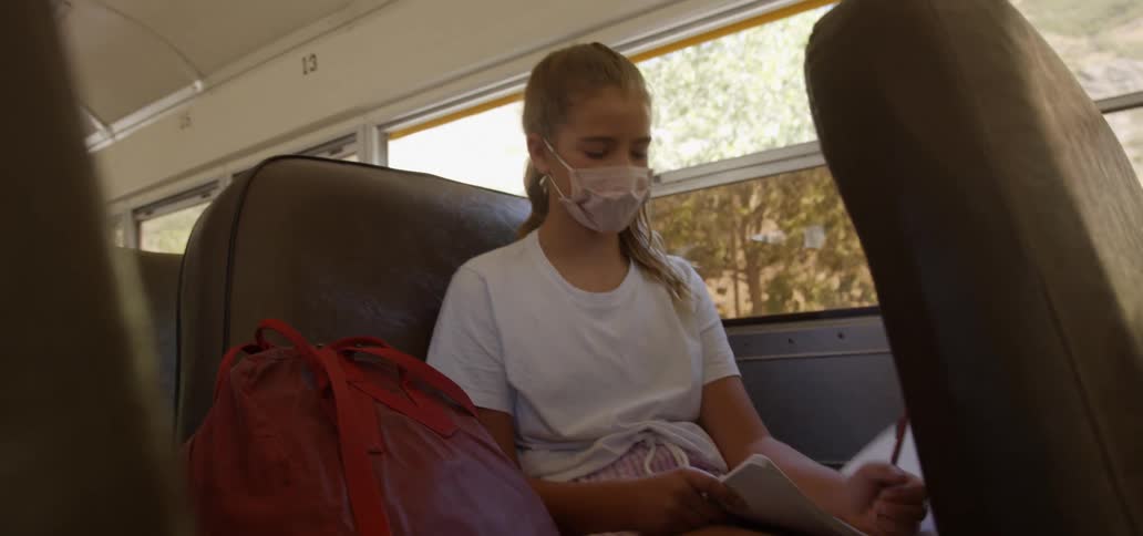 A girl is writing in her notebook as she rides the school bus