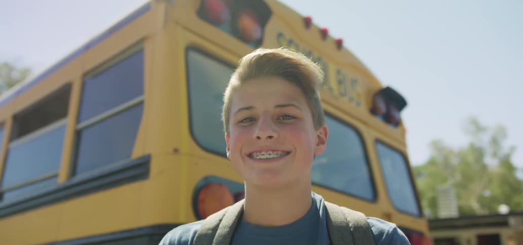 Male student with dental braces smiles broadly in front of school bus yellow