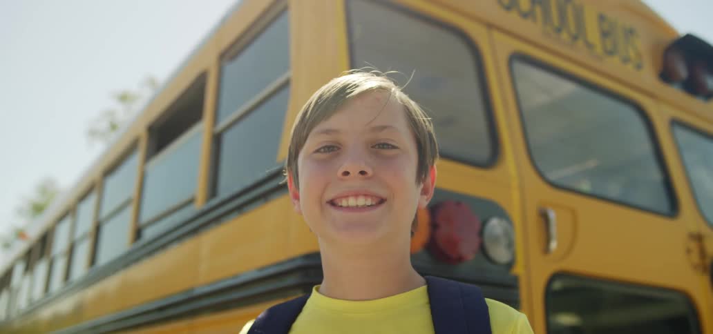 Child standing in front of a school bus smiling