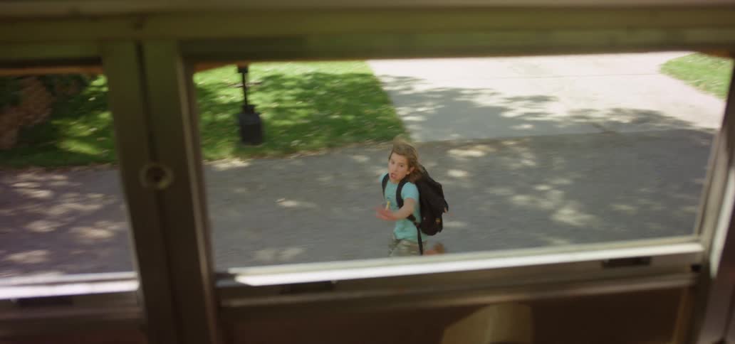A young boy runs outside of a school bus trying to catch up to it