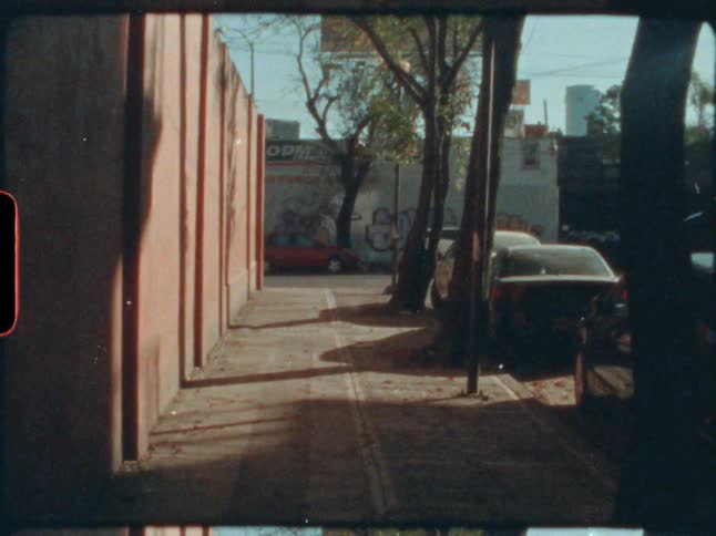 Vehicles are parallel parked on the side of a city street lined with trees