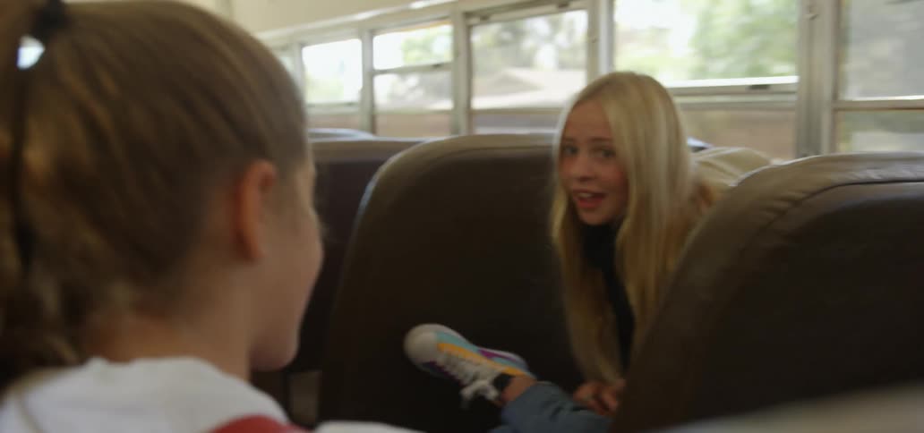 Two young girls talk together on a school bus