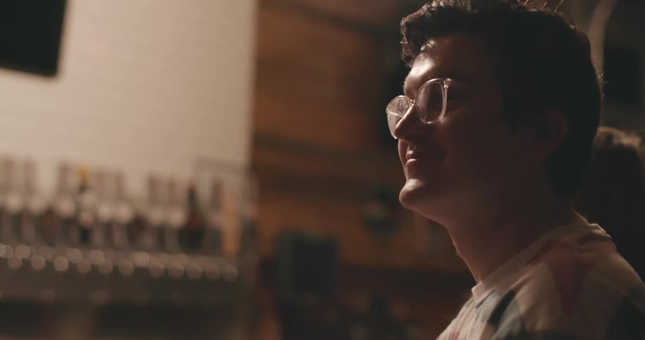 Young man wearing glasses looks relaxed and happy inside a bar