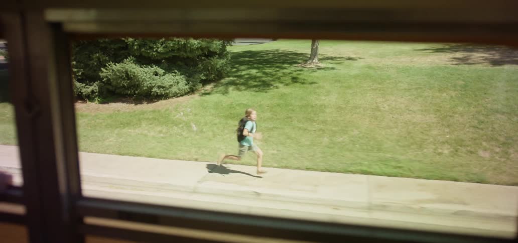 A girl laughs at boy running down the sidewalk chasing the school bus