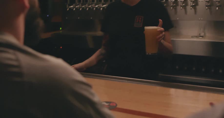A female bartender pours a beer and places it on the bar in front of a guest