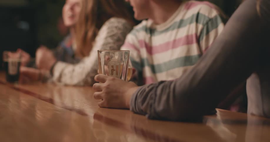 A woman talking to her friend at a bar top gives a man a finger when he looks at them
