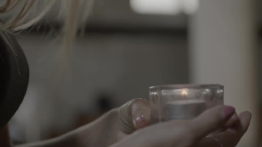 A woman holds and blows out a votive candle