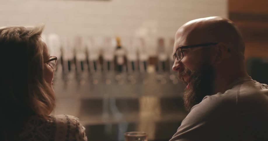 A man and woman sitting together in a bar talking and having a drink
