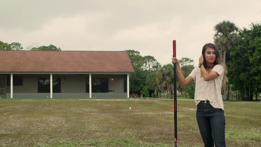 A young woman poses with a gardening tool in front of her ranch home in the country