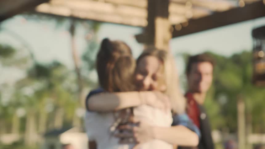 A woman running and hugging another woman with people sitting at a table in the background