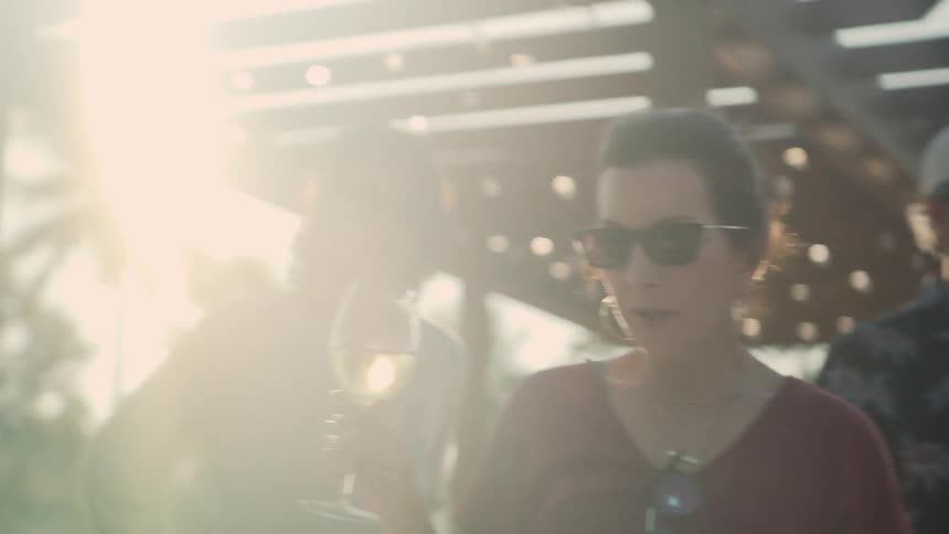 A woman drinks wine outdoors while standing with a group of men