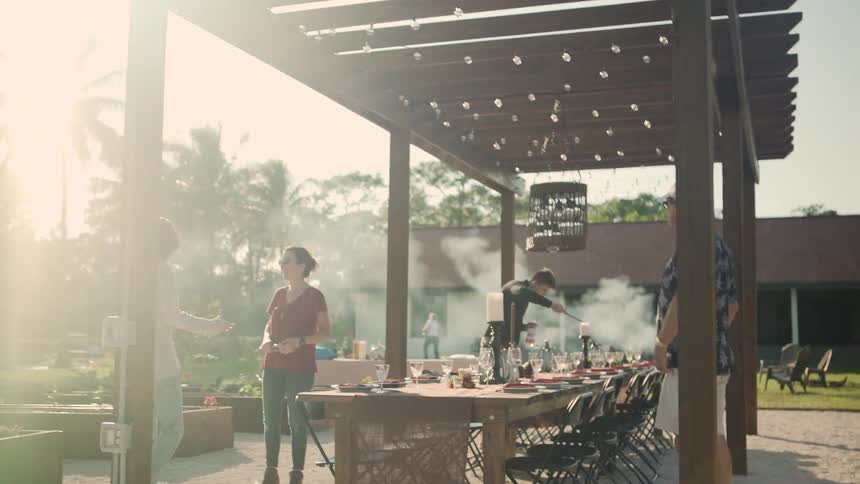 Family standing in a backyard grilling and chatting with each other