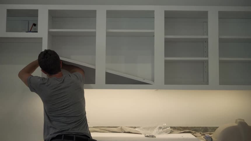 Man standing inside of a kitchen installing a shelf in new cabinets