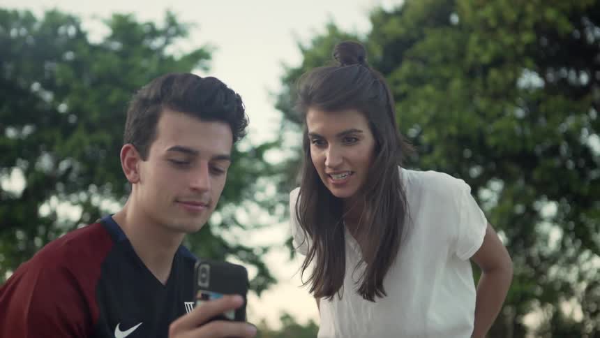 A brother and sister smile as they talk to someone in a video call while outside