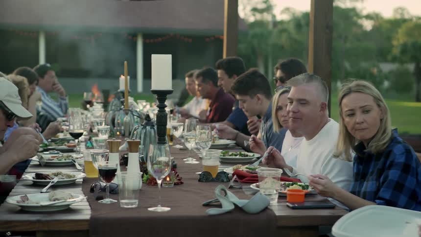 A group of people are sitting at a long table dining and have conversations while eating