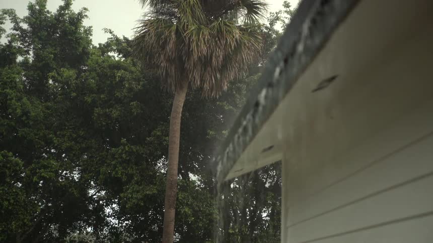 The side of a house as it rains with trees the sky and clouds in the background