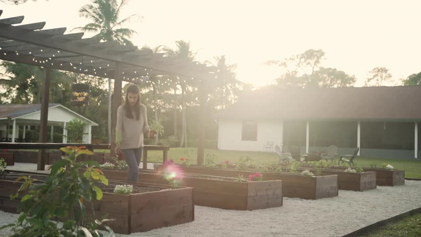 A woman tends to potted plants outside her home in a large boxed garden