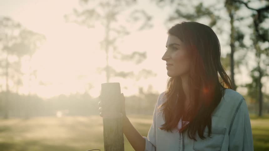 A young woman standing against a fence post in a rural area