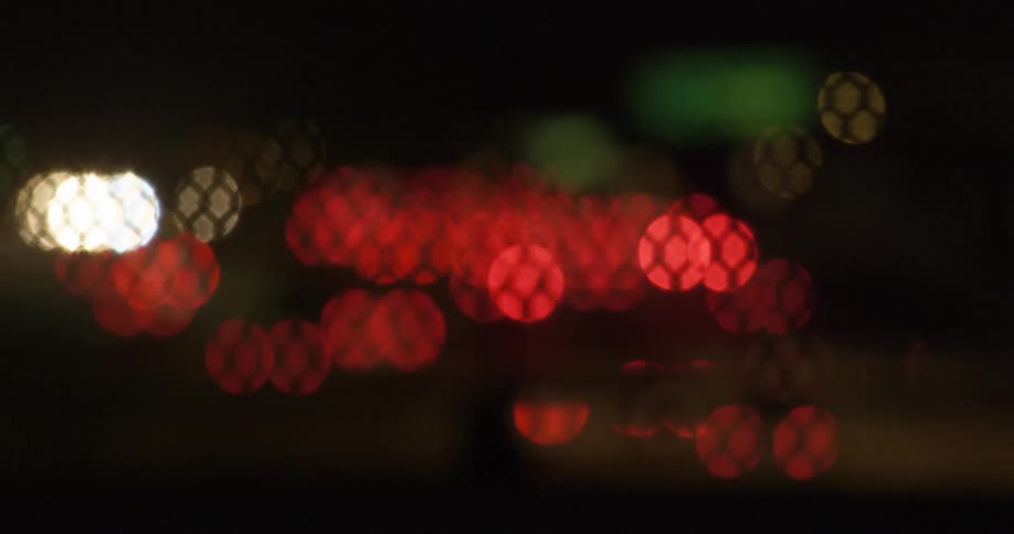 The red taillights of traffic blur seen through the grate of an overpass fence at night