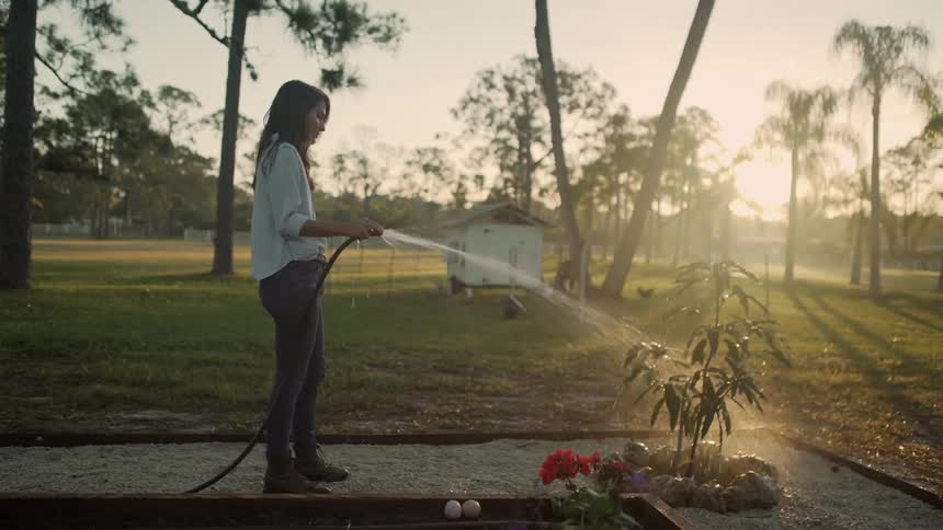 A woman is watering a plant in her yard