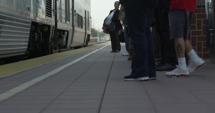 People stand at a train platform as a passenger rail leaves the station
