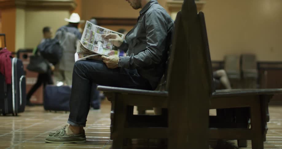 People pass time at a transit hub for a train by reading newspapers and walking around