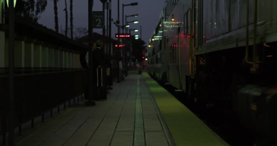 Passenger train approaching train station platform at night while a group of men wait