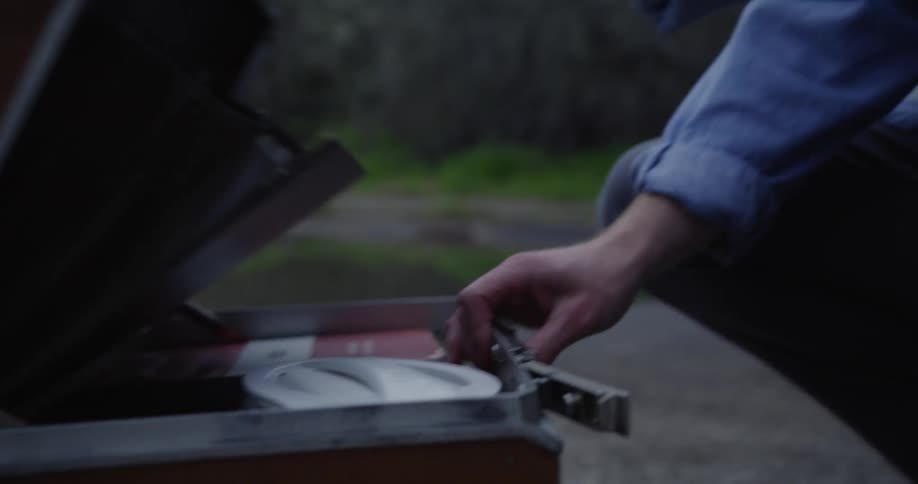 Man crouches outdoors near pond surrounded by leafless trees and opens briefcase