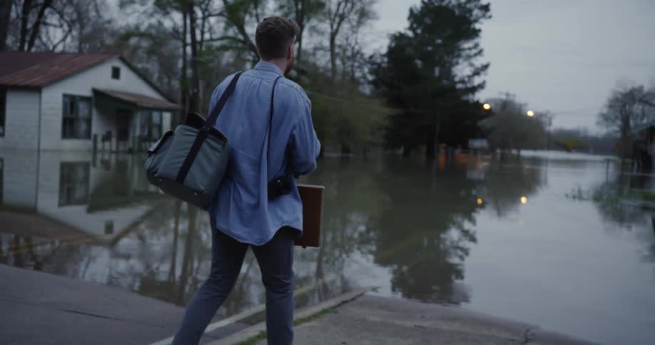 A man carries a cooler bag and briefcase to the end of a dock and kneels by the lake water