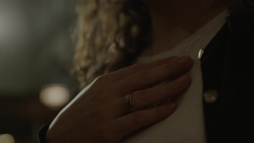 A woman lifts her hand to clasp a cross pendant she is wearing