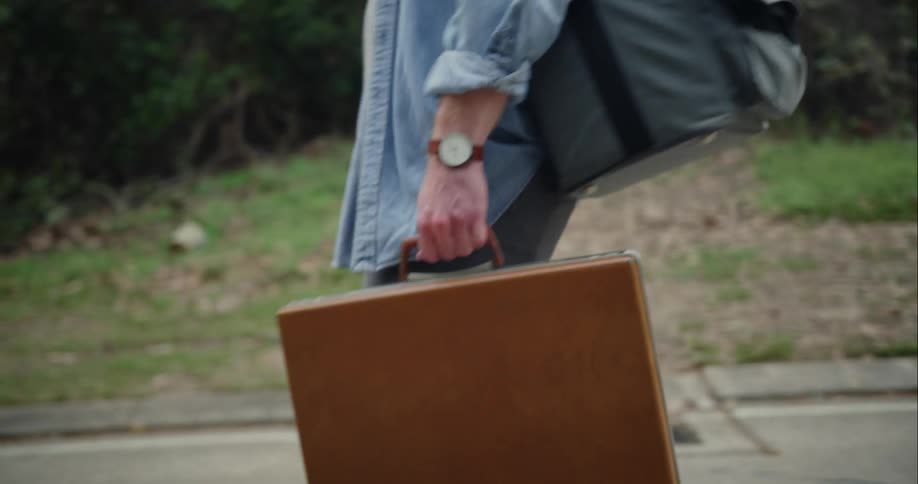 Man toting luggage walking down a road in daytime