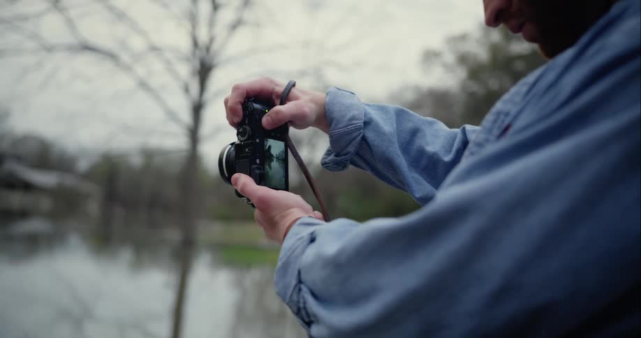 A man uses a digital camera to take photos of a pond and pavilion in the countryside
