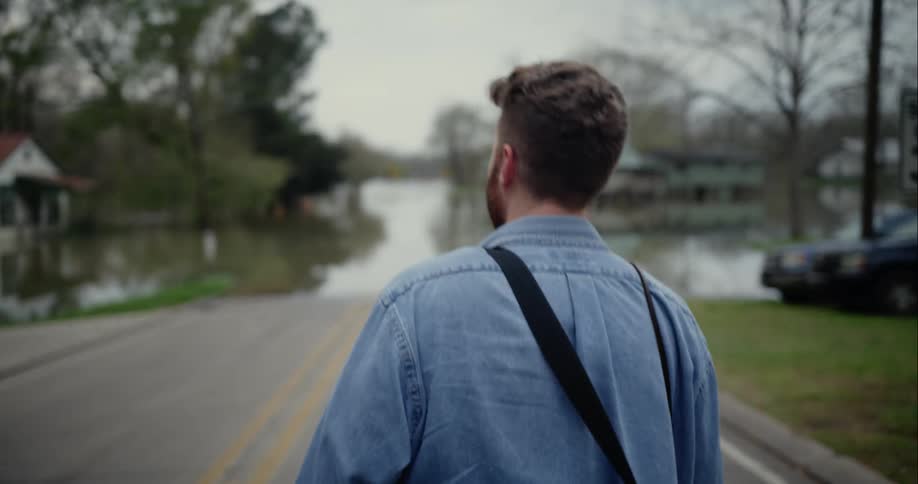 A man walks towards a flooded street in a neighborhood