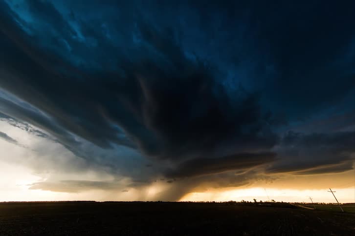 A road with vehicles near a grassy plain with lightning the sky and clouds above