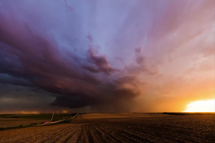 Lightning flashes in storm clouds above a rural field at sunset