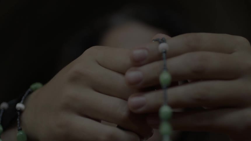 Two hands clasp a rosary