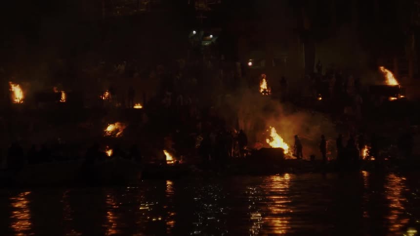 People standing on the shore as fires engulf a neighborhood