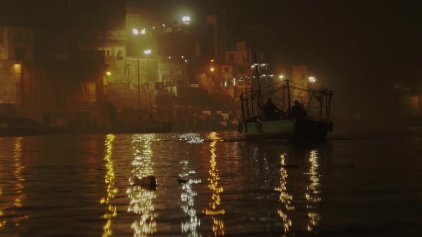 People sit in a boat that sails past buildings in a developing city at night