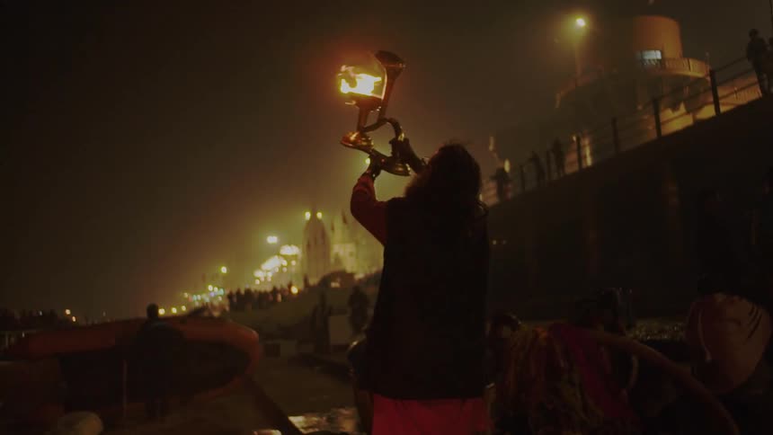 A person holding up a lamp with fire with the sky and streetlights in the background