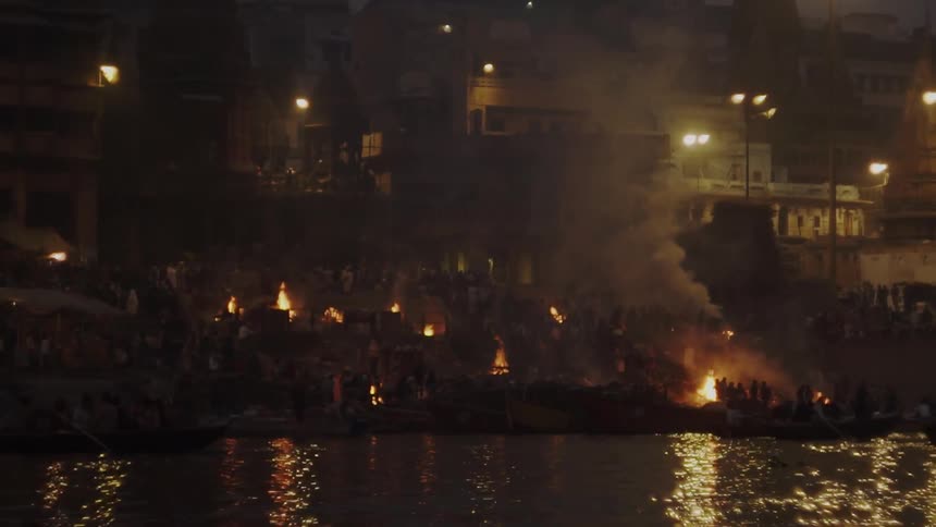 People standing outside next to large bonfires on the coast of city