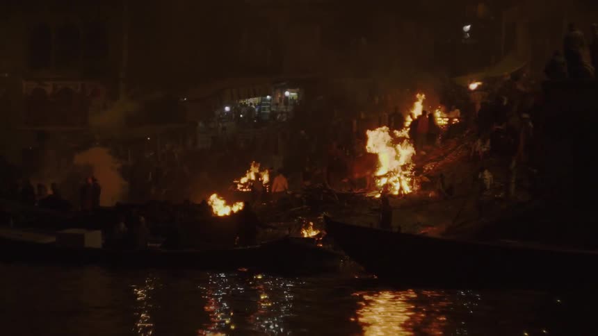 People standing next to a blaze of fire at night close to a river