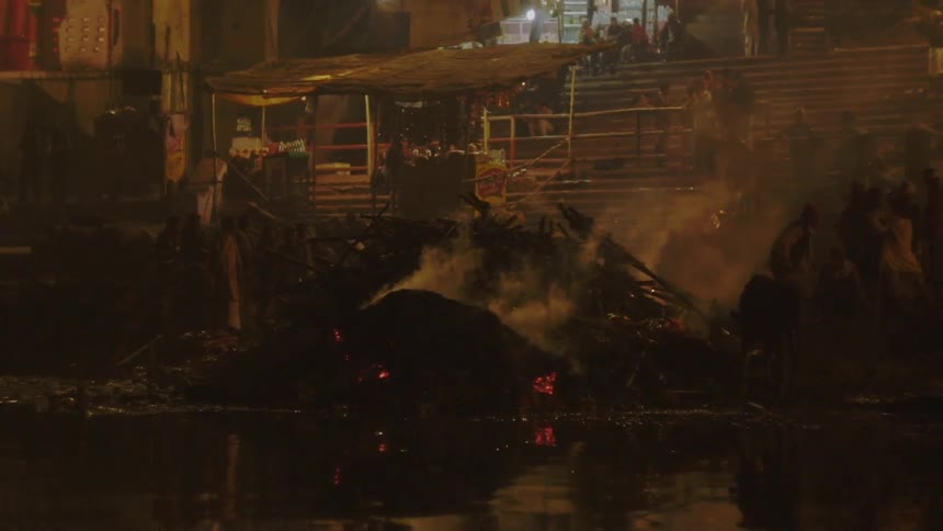 Smoke rises from burnt wreckage of metal near water as a group of people look on from above