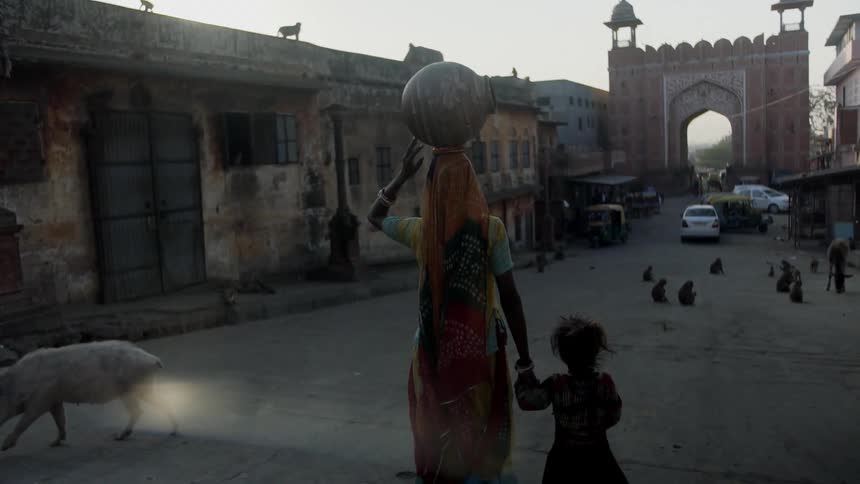 A woman balances a jug on her hand while holding a childs hand