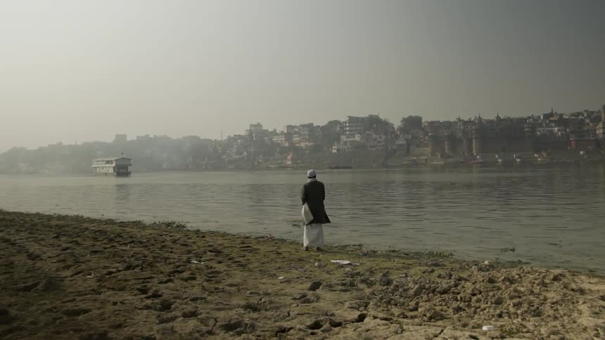Man standing next on the shore skipping rocks into the water