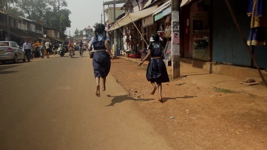 Two little girls run down a dirt road in a foreign town