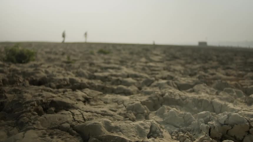 Dry cracked dirt on a desert floor with people walking in the distance