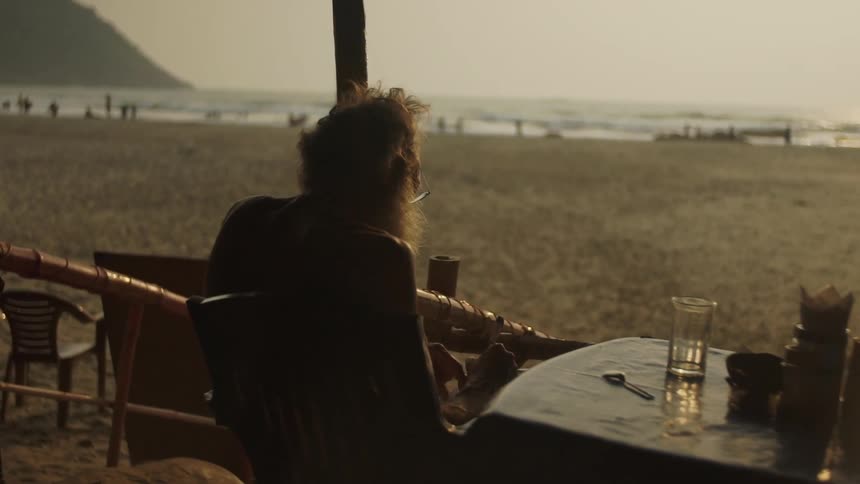 A man sits and writes at a beach side table
