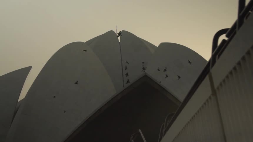 An opera house with a fence and birds flying with the sky and clouds in the background